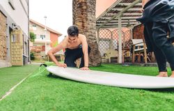 Male surfer in wetsuit waxing surfboard