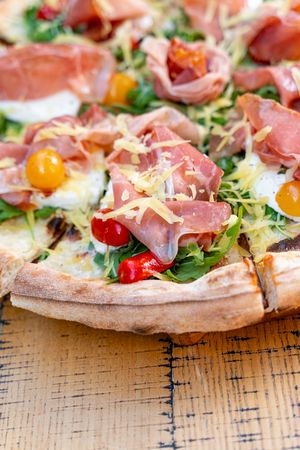 Gourmet Pizza with Prosciutto, Arugula, Yellow and Red Cherry Tomatoes on Rustic Wooden Table