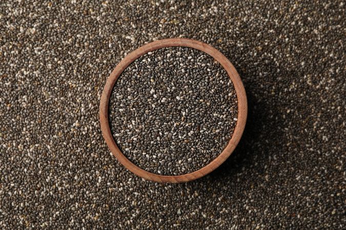 Wooden bowl and chia seeds on whole background, space for text