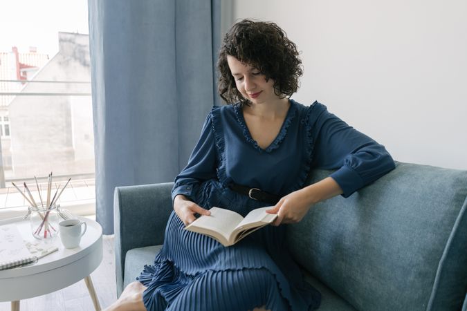 Young female reading book sitting on sofa