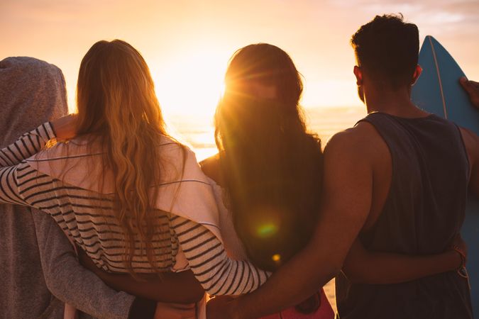 Rear view of group of friends standing together on beach watching sunset together