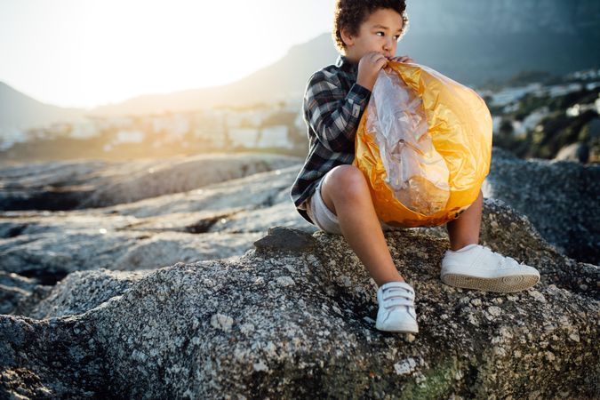 Child sitting on a rock filling air into an inflatable ball