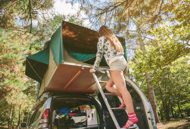Woman standing in ladder opening tent over car