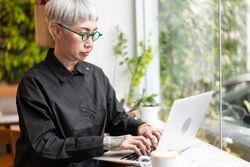 Older Asian woman watching and working on laptop at the coffee shop
