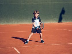 Happy child smiling while practicing tennis on clay court
