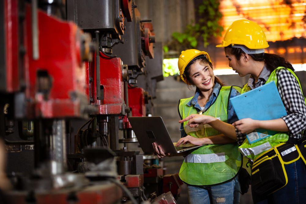 Two female engineers wearing PPR gear discussing project in factory