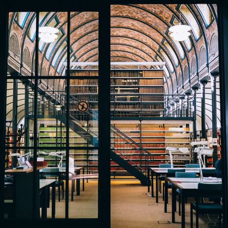 an opened door of a beautiful library with spring-color arranged of books in the bookshelves inside.