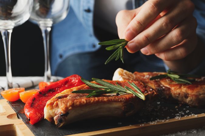 Person puts rosemary on steak. Composition with grilled food