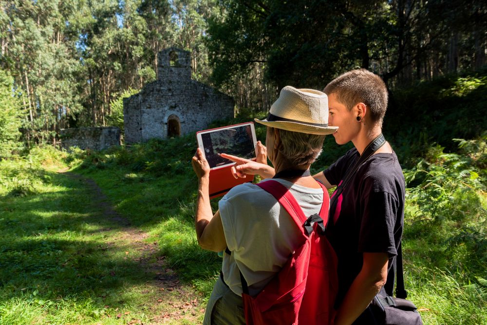 Younger woman hugging older woman taking picture on tablet in forest