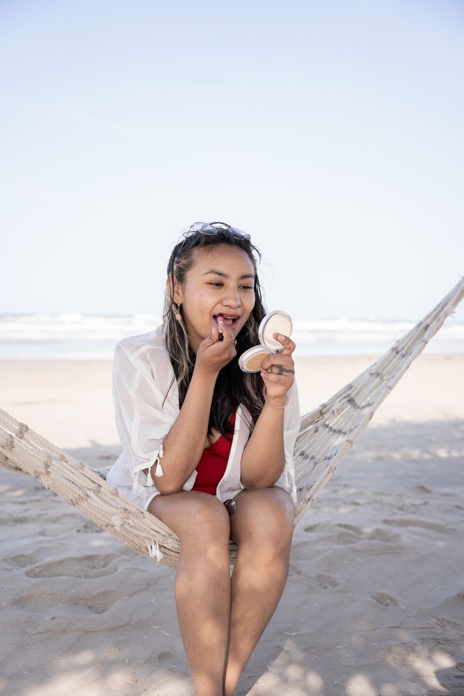 Hispanic woman applying lip balm on a hammock at the beach