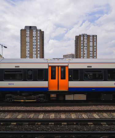 Centered shot of subway car with orange doors outside with buildings in background in London