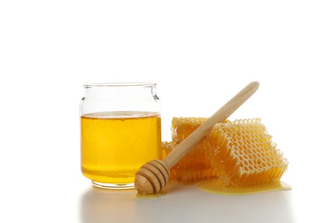 Pieces of honeycomb, glass jar and dipper isolated on studio background