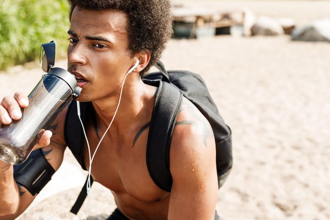 Black male wearing backpack hydrating after working out