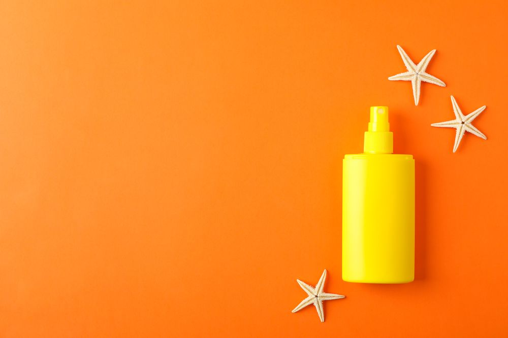 Composition with sunscreen spray and starfishes on color background, space for text. Summer vacation backdrop