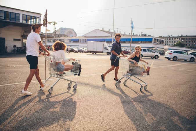 Two couples push shopping carts with one sitting in each