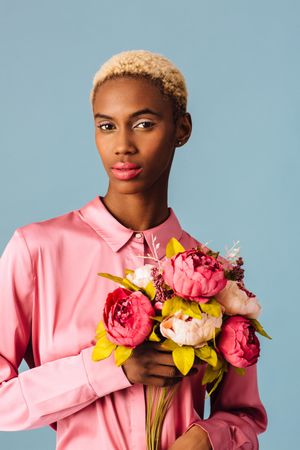 Black woman with short blonde hair holding bouquet of large pink flowers