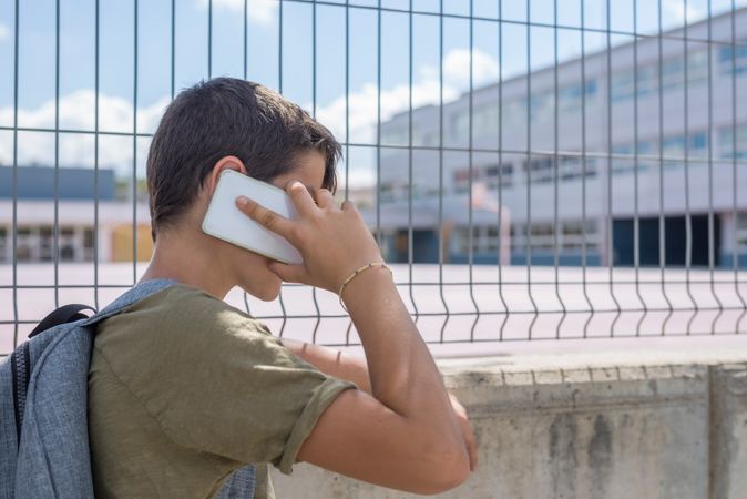 Side view of boy holding smartphone outside of school yard