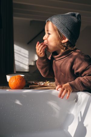 Hungry toddler eating fresh orange in kitchen