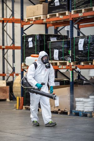 Man in PPE holding sanitizing machine in warehouse