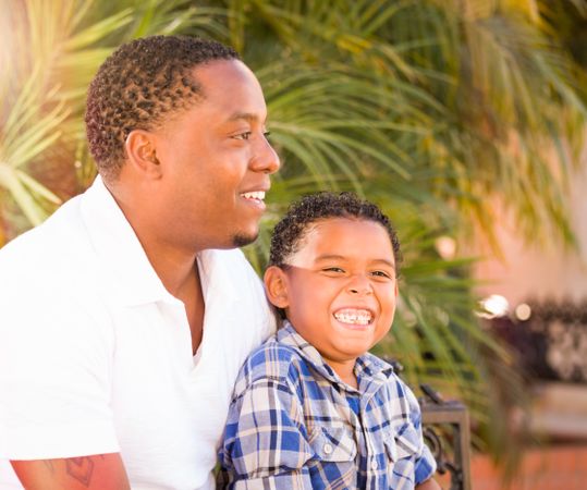 Black Father Sitting and Smiling With Son Outdoors