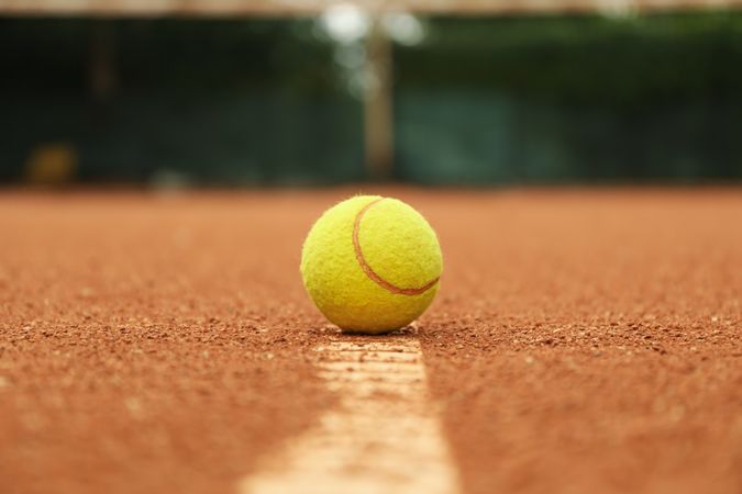 Light green tennis ball on clay court, close up