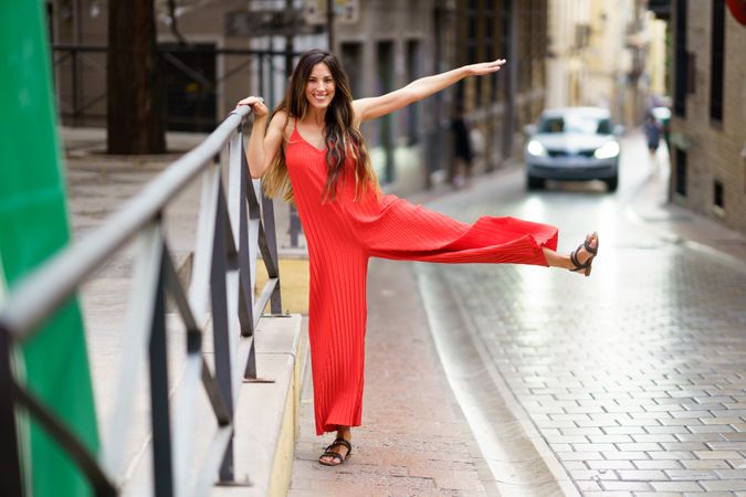 An Elegant Woman Dressed in a Stunning Red Dress Posing Gracefully on a Street Railing