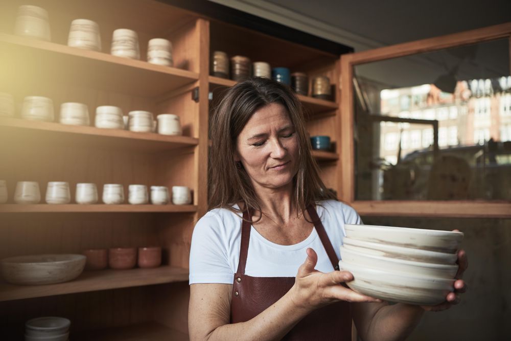 Woman in leather apron inspecting a stack of handmade plates