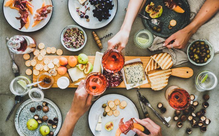 Charcuterie board with hands toasting with glasses of rose