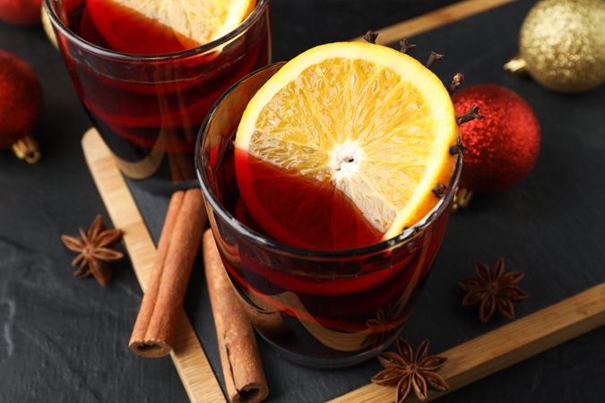 Glasses of tasty mulled wine and christmas baubles on dark background, close up