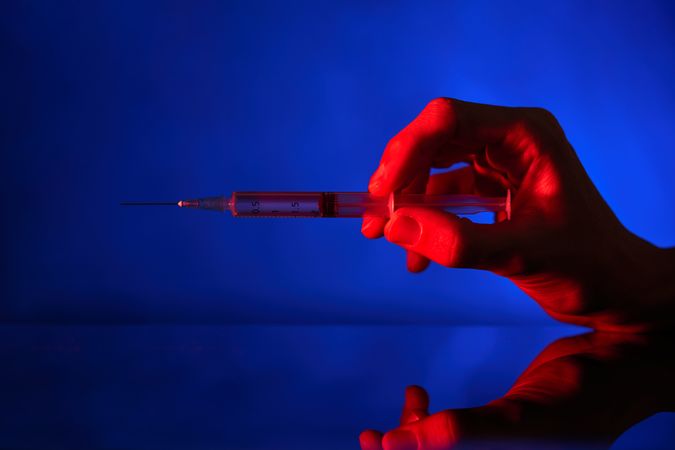 Unrecognizable person with syringe in neon lighting