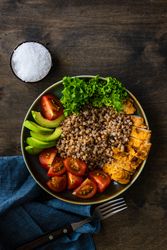 Healthy bowl of dinner with buckwheat, lettuce, avocado, and meat on wooden table