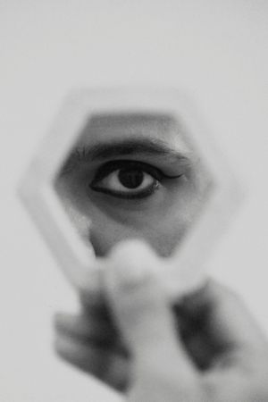 Grayscale photo of man looking at his eye in mirror