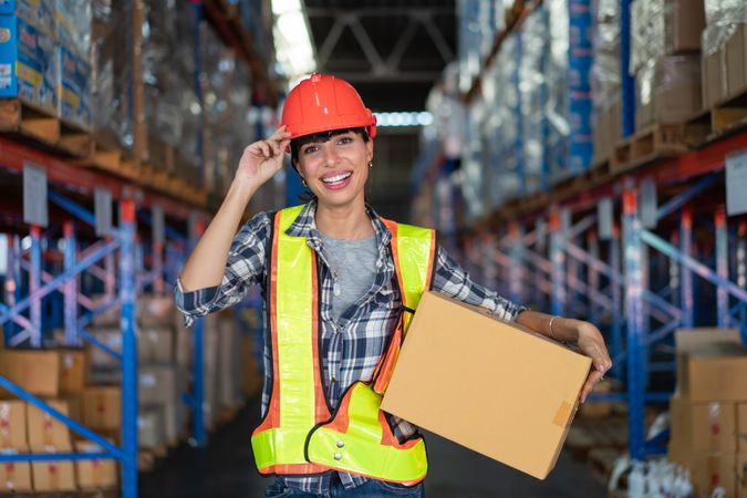 Woman in hard hat carrying in box in shipping center