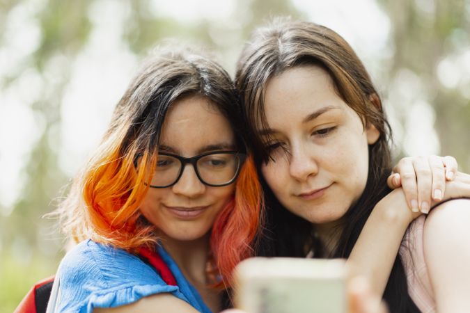 Two young woman hug each other while looking at the mobile phone to take a selfie