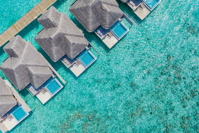 Aerial shot of patio pool of thatched beach villas in the sea