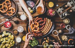 German sausages and pretzels displayed on wooden table with hands holding beer and pretzel 5lgpe0