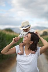 Adorable kid in hat on shoulders and looking at mother