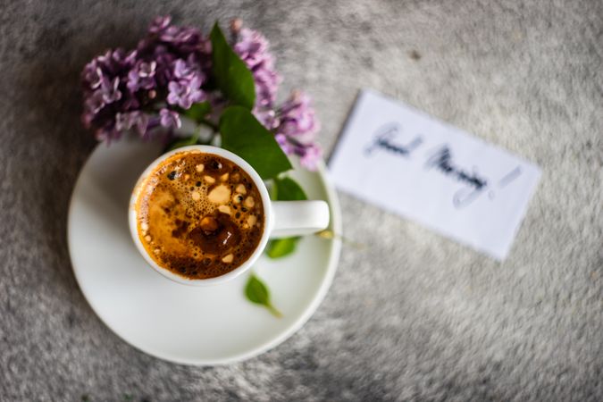 Top view of cup of espresso and lilacs on grey background with copy space