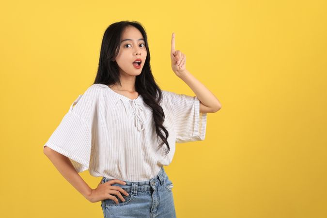 Portrait of Cheerful Asian Teenager with Long Hair and Casual Fashion, Pointing on Top for Copy Space