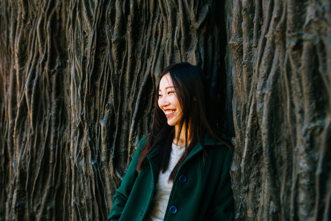 Cheerful Asian woman leaning on rough wall