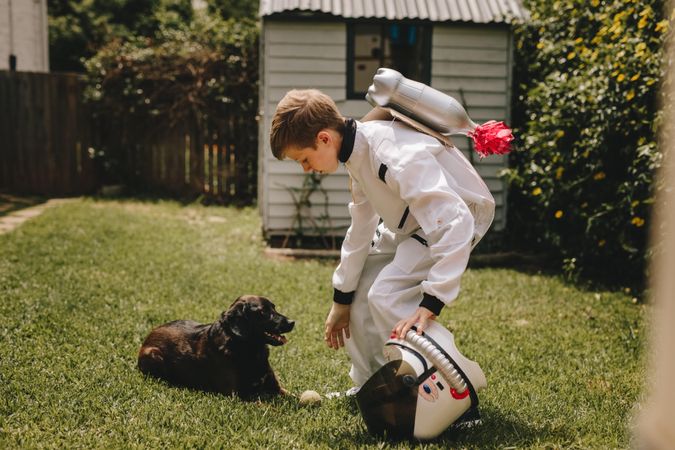 Small boy in an astronaut suit playing outside with his pet dog