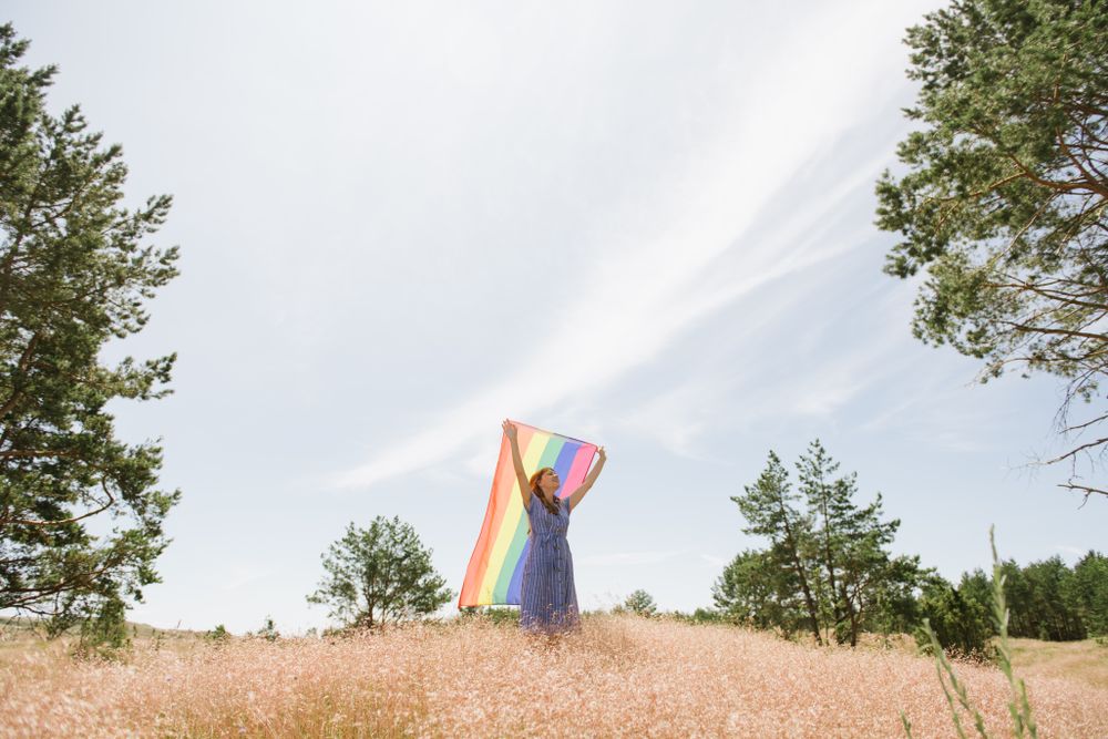 Young woman with rainbow banner against sky
