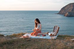 Woman reading on mat for picnic on seashore