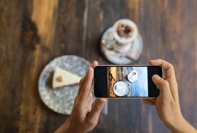 Faceless person taking picture of cake and coffee