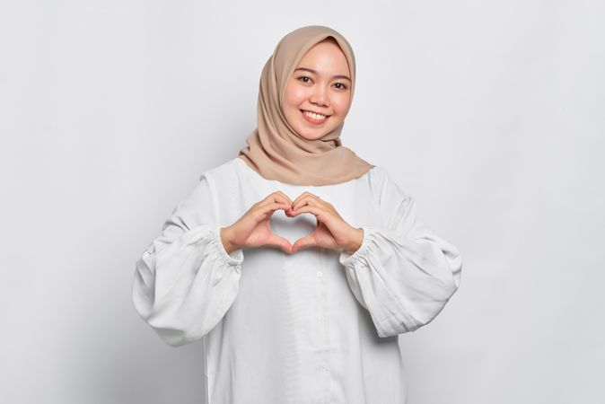 Muslim woman in headscarf and light blouse making heart with her hands