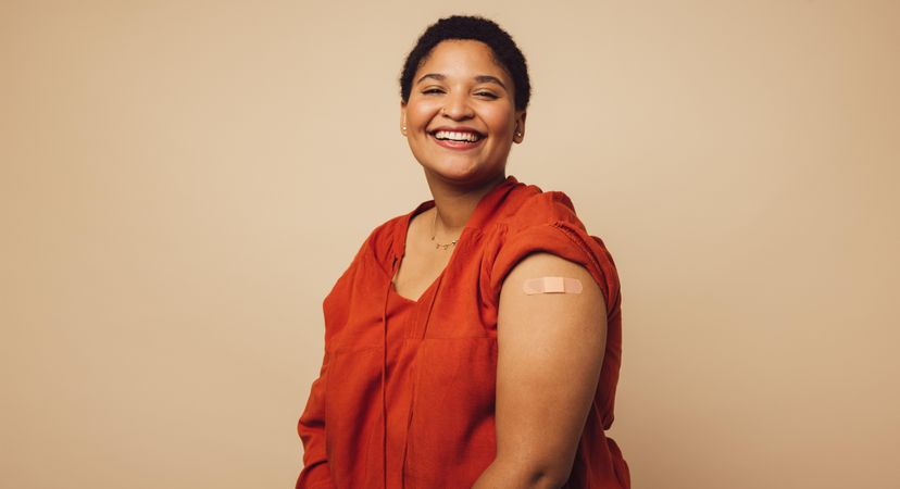 Woman looking happy after getting vaccine shot on brown background