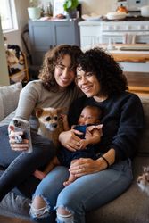 Family with dog and baby on sofa making video call, vertical