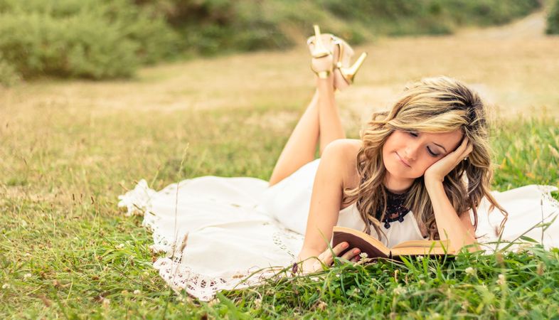 Romantic woman reading a book lying down outdoors