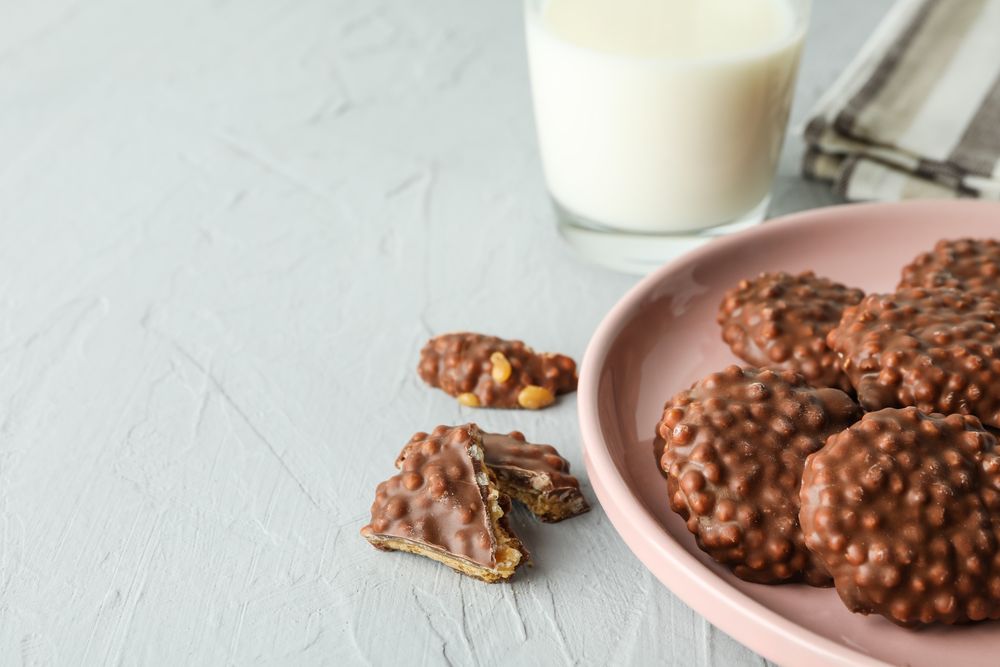 Plate with chocolate cookies and glass of milk on grey table, space for text