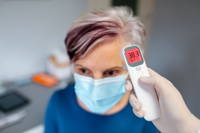 Mature woman with a fever whose temperature is taken by her doctor